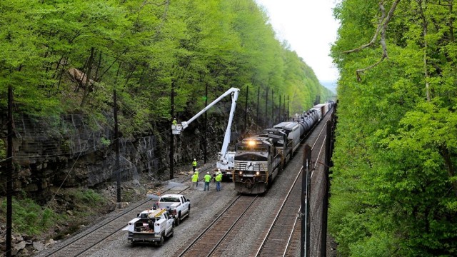 An eastbound mixed freight creeps past crews repairing the slide fence in the cut at Cassandra. The fence is electrified to "drop" red signals should a rock slide break through the fence and down onto the tracks. That has happened earlier and the crews are working hard to get Track One back on line. From the left, are Tracks One (eastbound), Two (both directions), and Three (westbound). Where the trucks are sitting used to be a fourth track that many have seen in older photos but was since removed years ago.