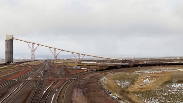 More coal loading. Far left is one of the many coal flood loaders in the area. The long conveyor leads to coal deposits; there are no underground mines here, it is all surface mining. The train in the center and right is an empty in the queue for the never-ending loader at the Black Thunder mine load out, seen in the previous photo. You will recall that the 125-car trains never stop in the loading process, but enter the yard empty and proceed through the loader, are filled, and depart, all without stopping. With the depressed coal industry (thanks to cheaper natural gas, low costs of crude oil, and lesser demand by foreign markets), what was once 100-plus trains departing daily has been reduced to sometimes fewer than 30 trains a day. Fossil fuels reign in the area; it’s not uncommon to see large oil pumping rigs right across the road from the open pit coal mines.